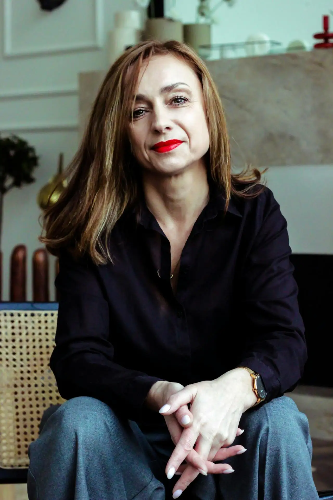 Retrato de uma mulher sentada em ambiente interno, usando blusa preta, com cabelo castanho e batom vermelho, olhando para a câmera.